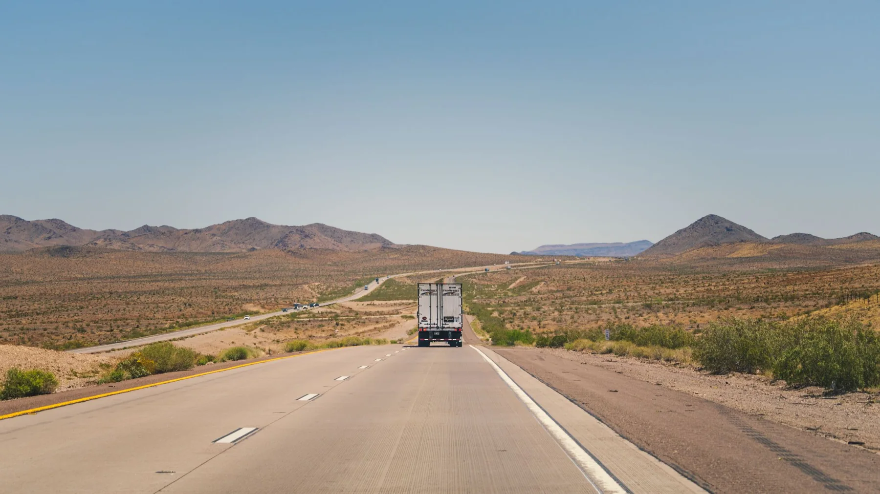 A freight truck traveling on a sunlit highway through the Arizona desert.